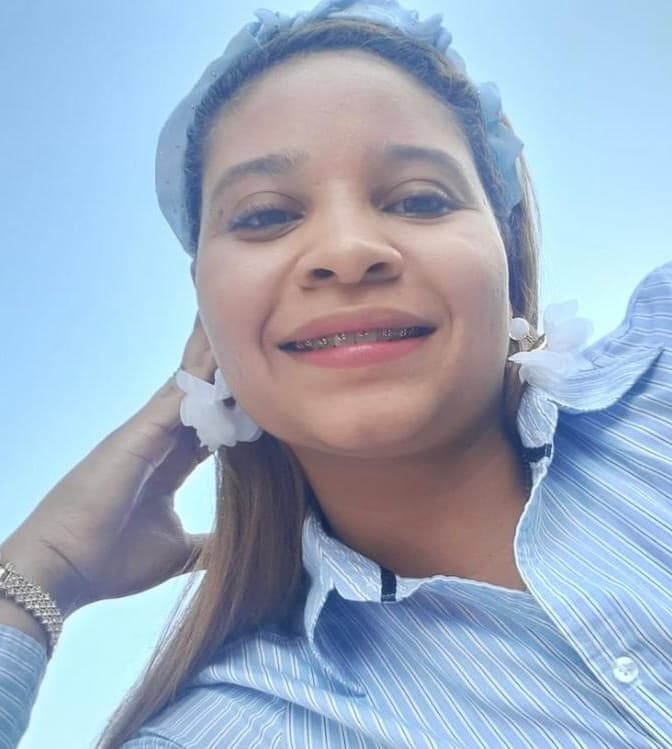 Mujer sonriente con brackets, camisa de rayas azules y diadema azul bajo un cielo despejado.