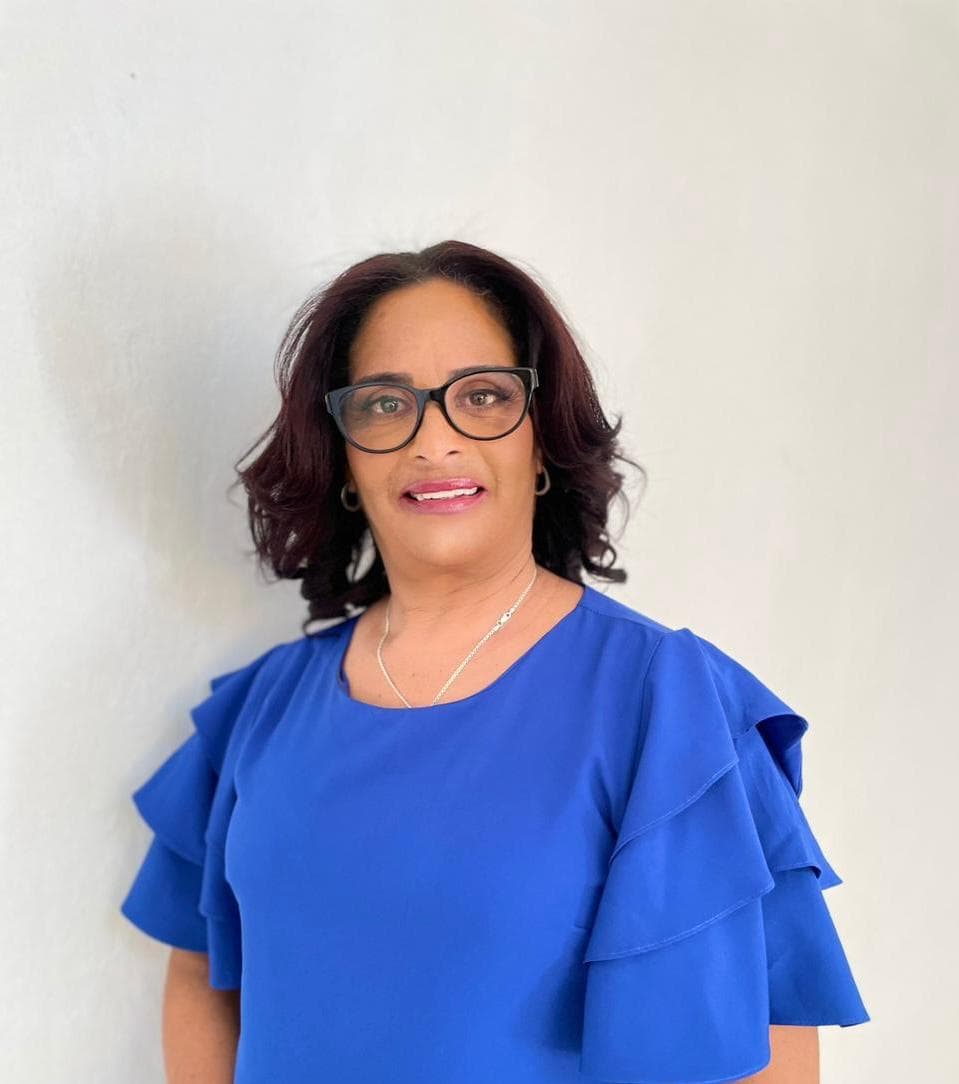Mujer con gafas y blusa azul de volantes posando frente a un fondo blanco.