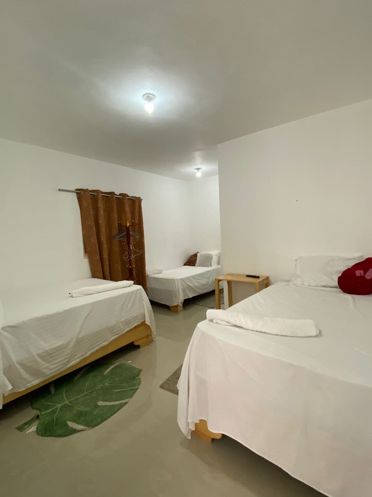 Tres camas individuales con sábanas blancas en un dormitorio luminoso con alfombra de hoja verde.