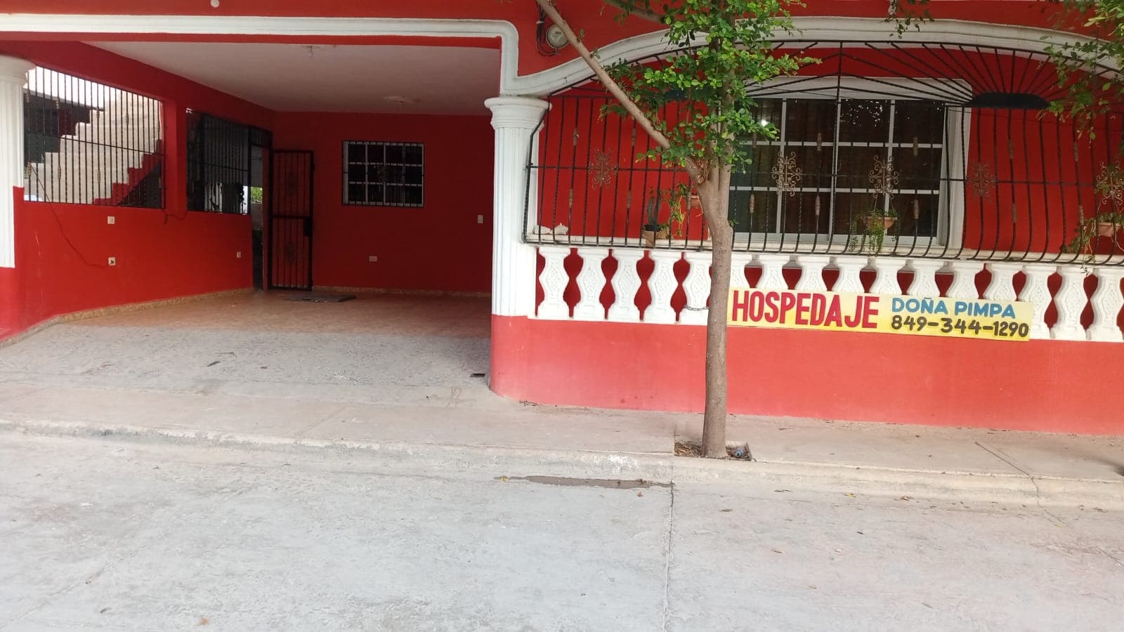 Fachada roja con balcón blanco, rejas negras y un letrero de Hospedaje Doña Pimpa.