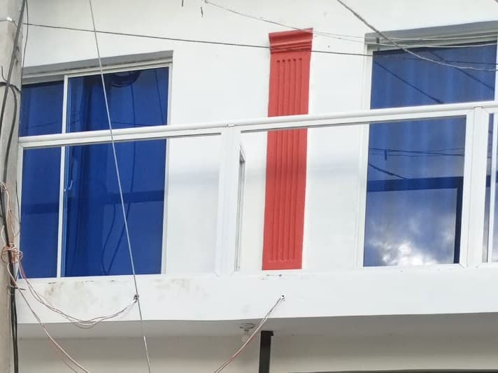 Fachada blanca con ventanas de vidrio azul, barandilla blanca y una columna roja decorativa central.